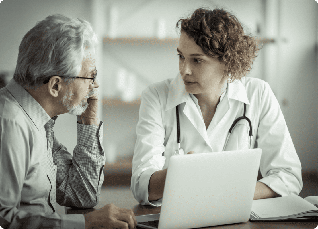 A female doctor is educating an old man patient about his health condition through the EMR system on her labtop